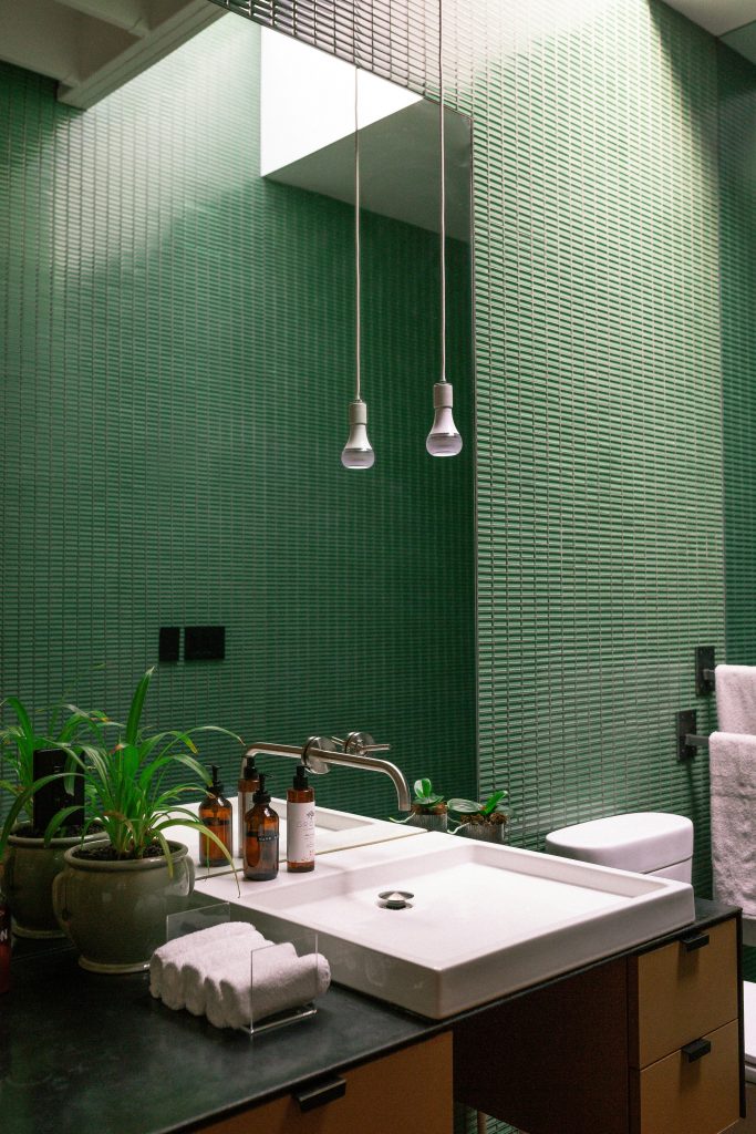 Contemporary bathroom featuring a green tiled wall, plants, sink, and towels.