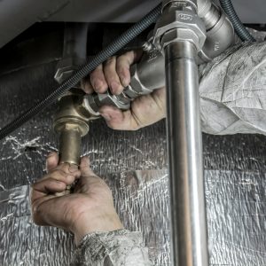 Close-up of a plumber's hands installing steel pipes indoors, showcasing skilled manual work.